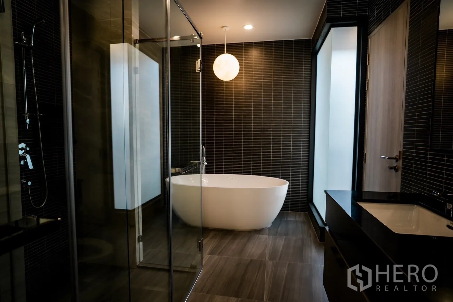 Detached House for rent or sale in Bang Kapi, Bangkok - Contemporary bathroom with freestanding soaking tub, glass shower and dark tile finishes.