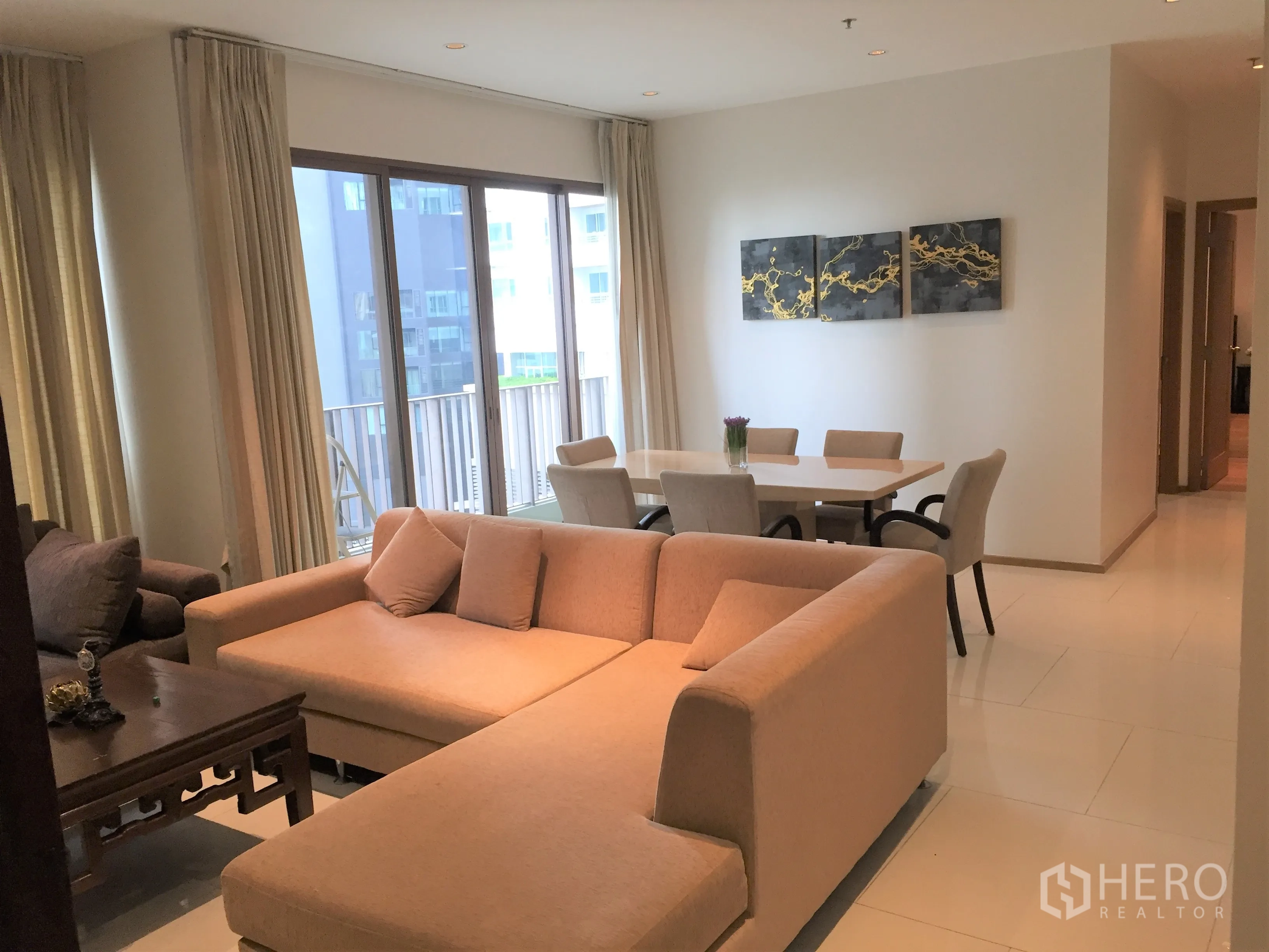 Condominium for rent in Khlong Toei, Bangkok - Bright living and dining area with an L-shaped sofa, balcony access and floor-to-ceiling windows.