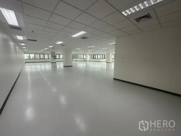 Office Space for rent in Bang Rak, Bangkok - Empty office suite showing an open layout, ceiling-mounted lights, and expansive windows on two sides.