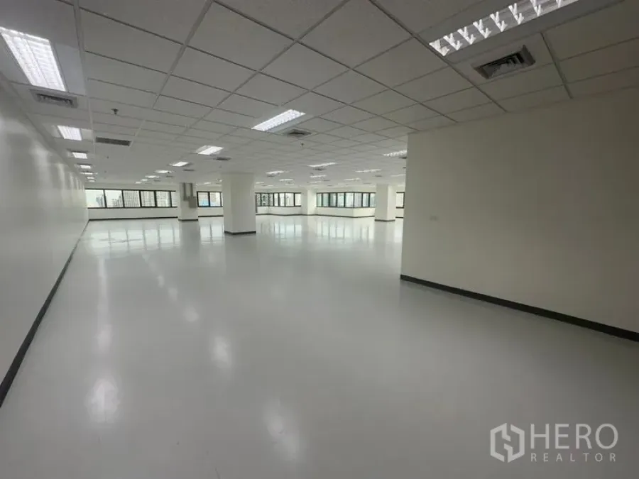 Office Space for rent in Bang Rak, Bangkok - Empty office suite showing an open layout, ceiling-mounted lights, and expansive windows on two sides.