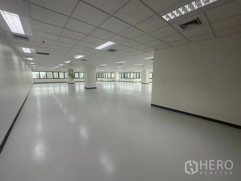 Office Space for rent in Bang Rak, Bangkok - Empty office suite showing an open layout, ceiling-mounted lights, and expansive windows on two sides.