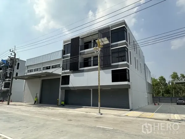 货栈 出租在Bang Phli, Samut Prakan - 现代三层仓库外立面，深色窗格与多扇卷闸门。