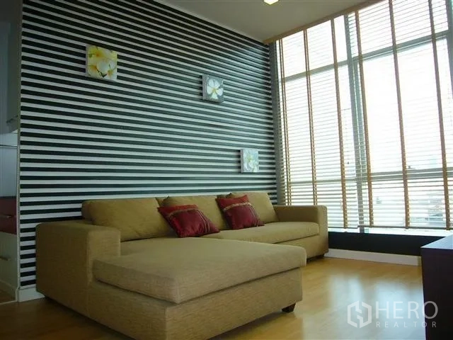 Condominium for rent in Khlong San, Bangkok - Living room with L-shaped sofa, striped feature wall and tall window blinds.