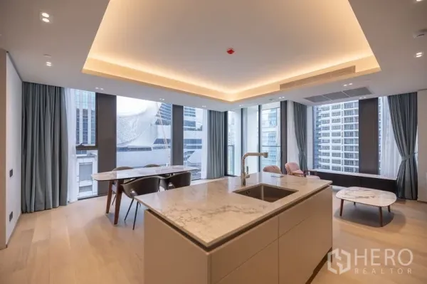 Condominium for rent in Pathum Wan, Bangkok - Kitchen island with sink and marble countertop facing a bright dining area and tall windows.