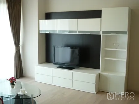 Condominium for rent in Watthana, Bangkok - Modern living area featuring a white TV console with shelving beside a large window.