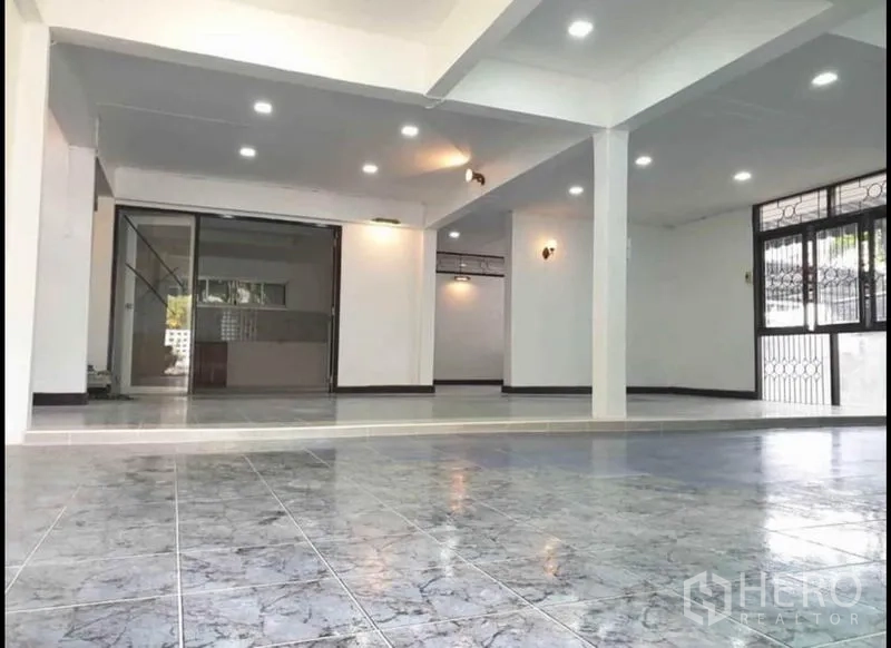 独立式住宅 出租在Lat Phrao, Bangkok - 明亮客厅，嵌入式照明、立柱与大窗户，通向厨房区域。