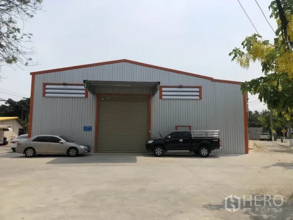 Warehouse for rent in Bang Yai, Nonthaburi - Front elevation of the warehouse featuring a large roller shutter door, canopy and ample driveway parking.