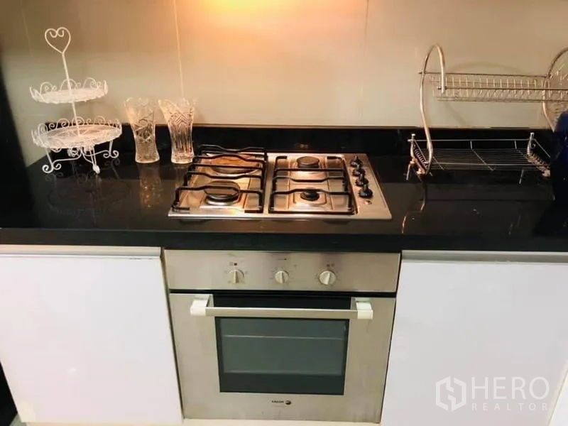 Detached House for rent in Watthana, Bangkok - Close-up of a built-in gas stove and oven on a black countertop under warm lighting.