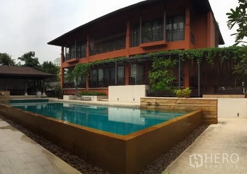 Detached House for rent in Khlong Toei, Bangkok - Low-rise villa building with greenery facing a modern rectangular swimming pool and pool deck.