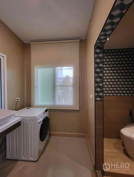 Townhouse for rent or sale - Laundry area with front-loading washing machine beside a bathroom with patterned tiles and a frosted window.