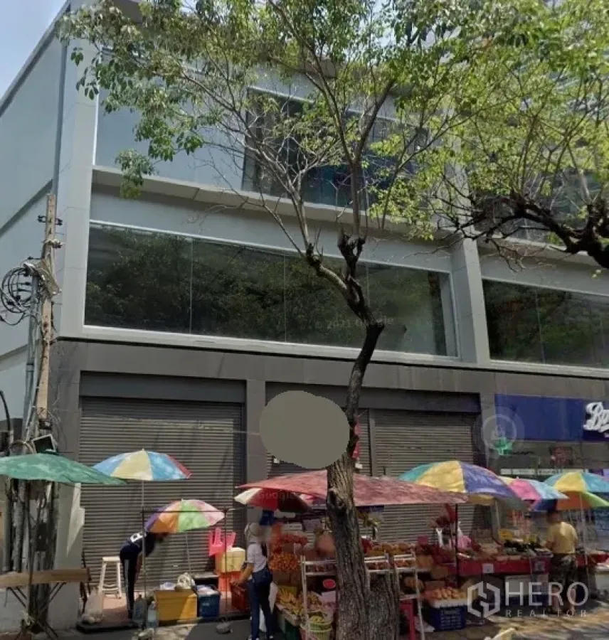 พื้นที่ขายปลีก ให้เช่าในWatthana, Bangkok - อาคารค้าปลีกหน้าถนน กระจกบานใหญ่ ประตูม้วน หน้าอาคารมีร่มขายของหลากสี ใต้ต้นไม้ ในย่านวัฒนา กรุงเทพฯ