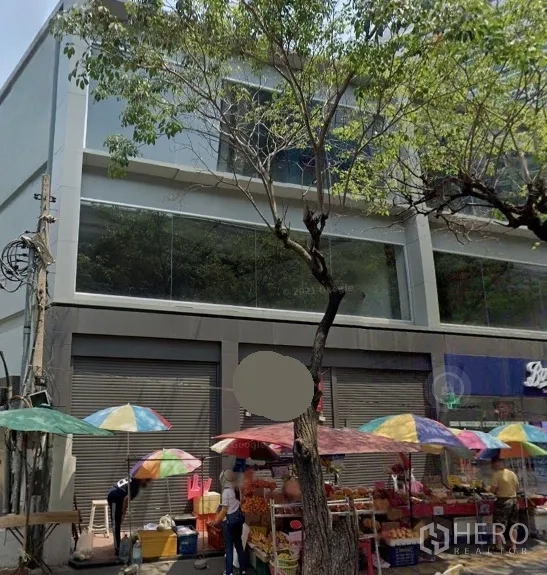 พื้นที่ขายปลีก ให้เช่าในWatthana, Bangkok - อาคารค้าปลีกหน้าถนน กระจกบานใหญ่ ประตูม้วน หน้าอาคารมีร่มขายของหลากสี ใต้ต้นไม้ ในย่านวัฒนา กรุงเทพฯ