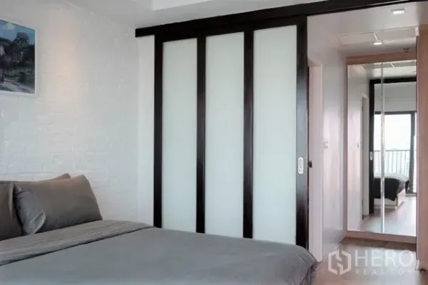 Condominium for rent in Khlong Toei, Bangkok - Bedroom with sliding frosted-glass wardrobe doors and hallway mirror leading to the balcony.