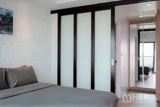 Condominium for rent in Khlong Toei, Bangkok - Bedroom with sliding frosted-glass wardrobe doors and hallway mirror leading to the balcony.
