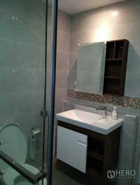 Condominium for rent in Khlong Toei, Bangkok - Modern bathroom with glass-enclosed shower, vanity and grey tiles.