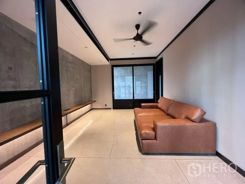 Condominium for rent in Sathon, Bangkok - Cozy media room with leather sofa, ceiling fan and minimalist concrete walls.