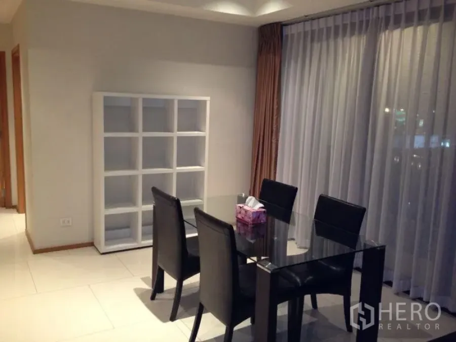 Condominium for rent or sale in Khlong Toei, Bangkok - Dining area with a glass table, four black chairs, floor-to-ceiling curtains, and a white cube shelf.