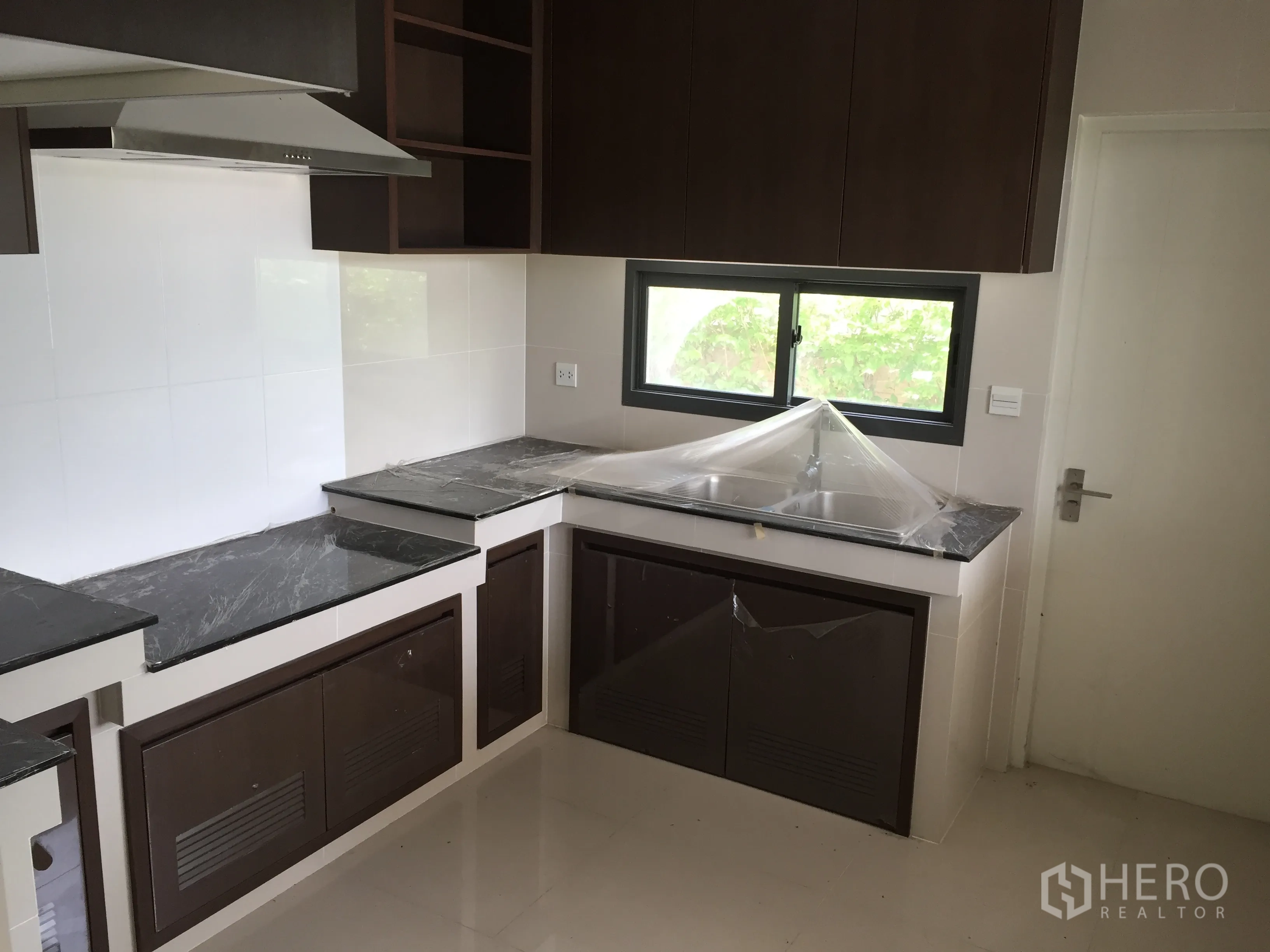 独立式住宅 出租或出售在Prawet, Bangkok - 配备深色石材台面与吊柜的整体厨房，带窗通风。