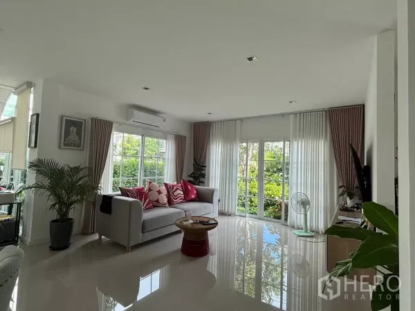 独立式住宅 出租在Prawet, Bangkok - 采光充足的客厅，大窗与窗帘，配沙发，面向绿景。