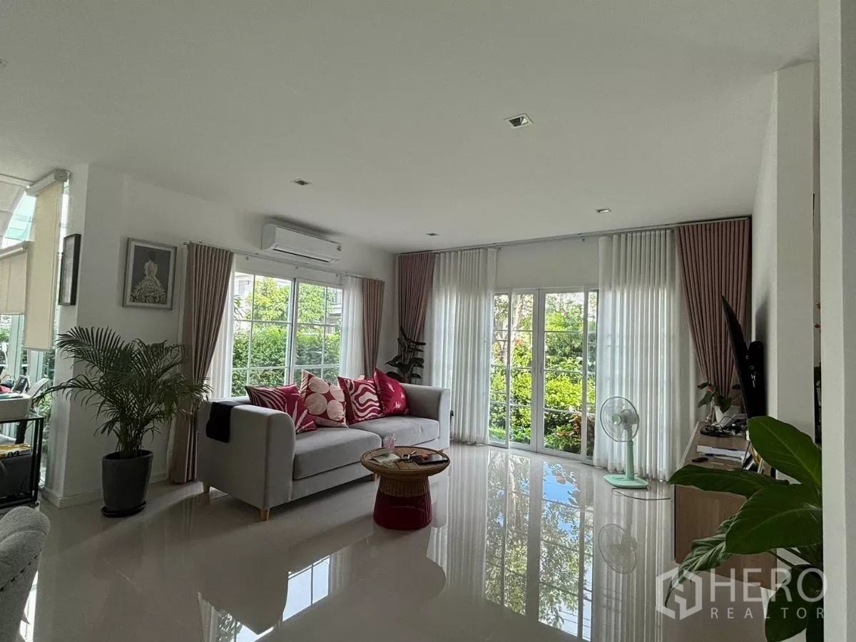 独立式住宅 出租在Prawet, Bangkok - 采光充足的客厅，大窗与窗帘，配沙发，面向绿景。