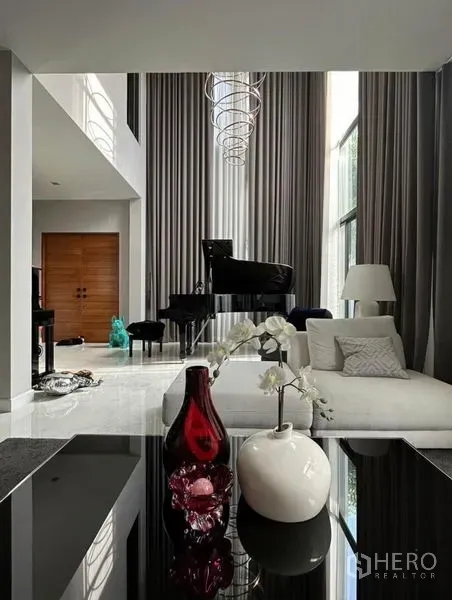 Detached House for rent - Double‑height living room with floor‑to‑ceiling curtains, modern chandelier, white sofa and grand piano.