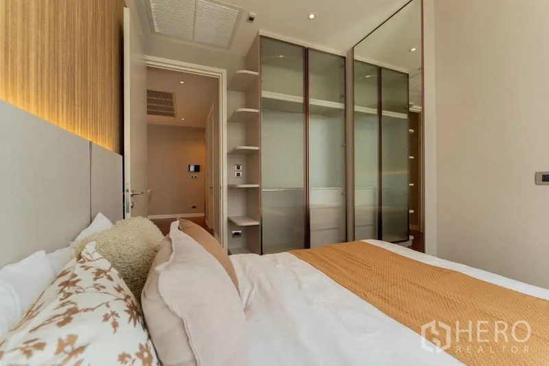 Condominium for rent in Watthana, Bangkok - Second bedroom with fitted wardrobes, open shelves and warm bedding tones.