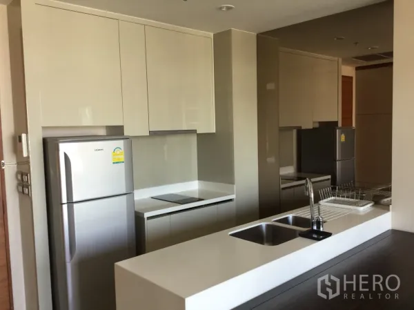 Condominium for rent in Khlong Toei, Bangkok - Contemporary kitchen with glossy cabinets, island with double sink and stainless fridge.