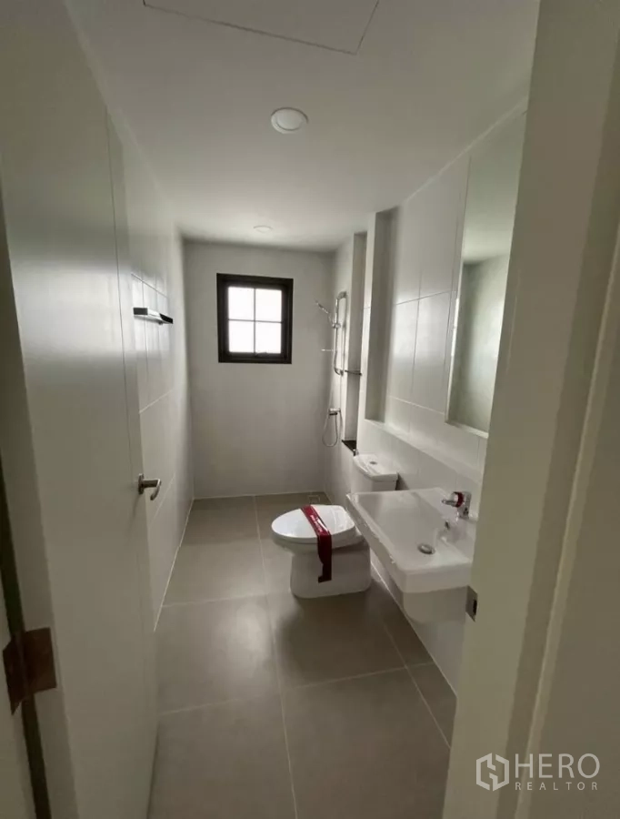 Detached House for rent in Bang Phli, Samut Prakan - Long bathroom with window, shower and vanity in light tiles.