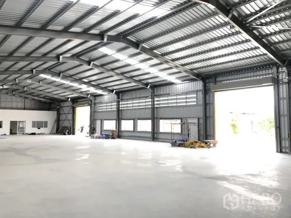 Warehouse for rent in Nonthaburi - Spacious warehouse interior with high steel truss roof, skylights, large shutter openings and polished concrete floor.