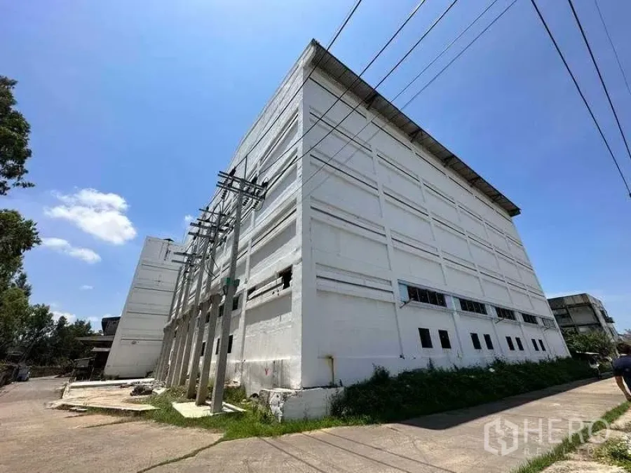 工厂 出租在Mueang Samut Prakan, Samut Prakan - 北榄市区多层白色厂房外观，临近电线杆，天空晴朗。