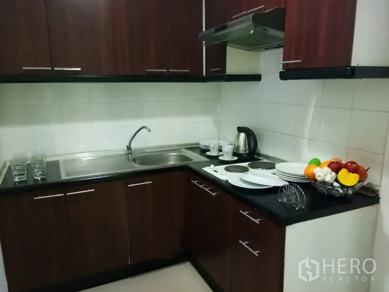 คอนโด ให้เช่าในWatthana, Bangkok - ครัวรูปตัวแอลขนาดกะทัดรัด ตู้ลายไม้เข้ม เตาไฟฟ้า เครื่องดูดควัน และอ่างล้างจานคู่