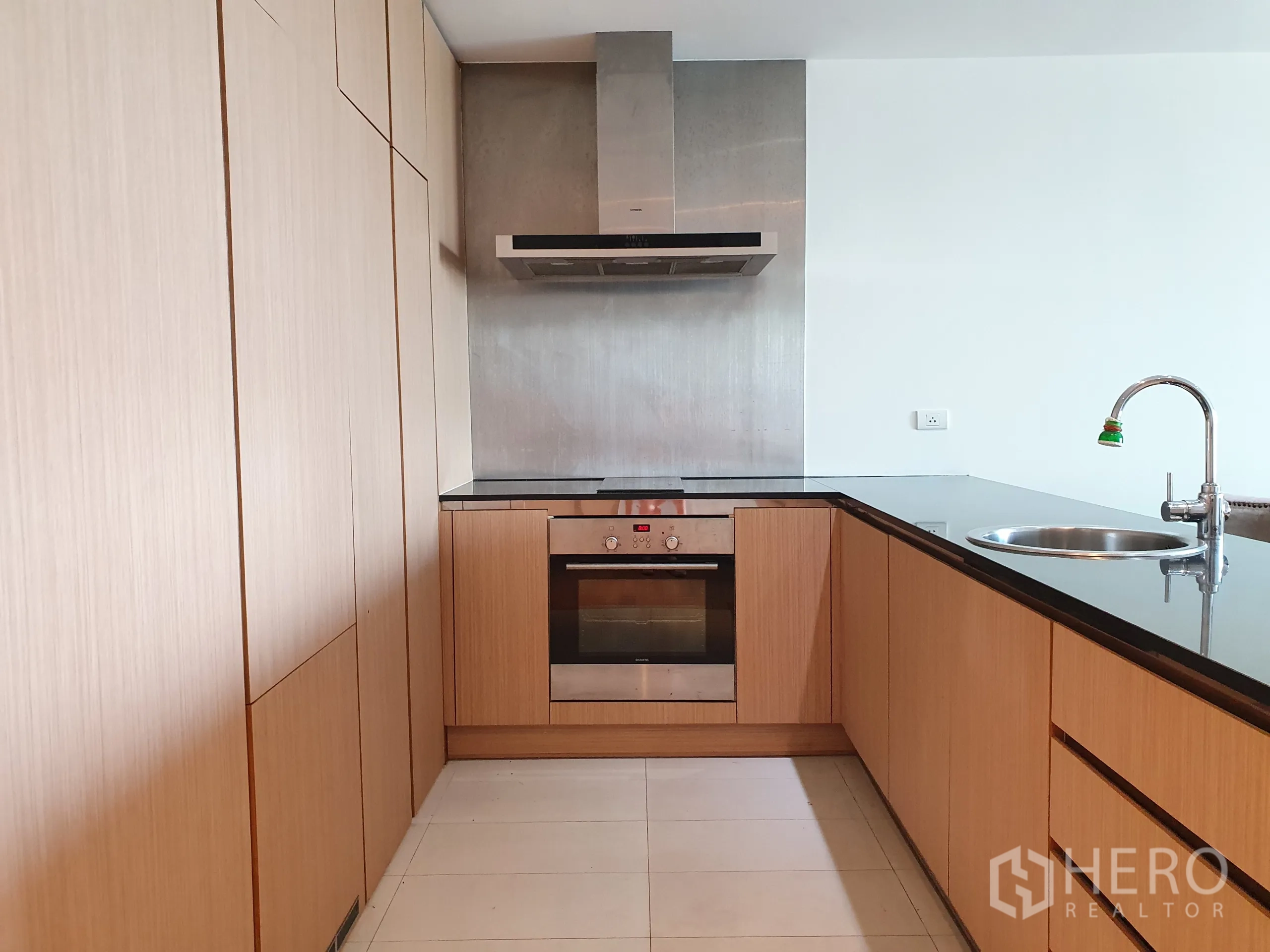 公寓 出租或出售在Yan Nawa, Bangkok - L 型厨房，木质橱柜与黑色台面，配烤箱、灶台与抽油烟机。