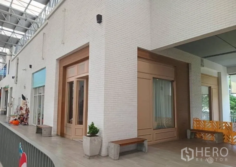 Retail Space for rent in Khlong Toei, Bangkok - Modern retail arcade with white brick walls, skylight roof, and a shopfront with tall wooden doors and benches.