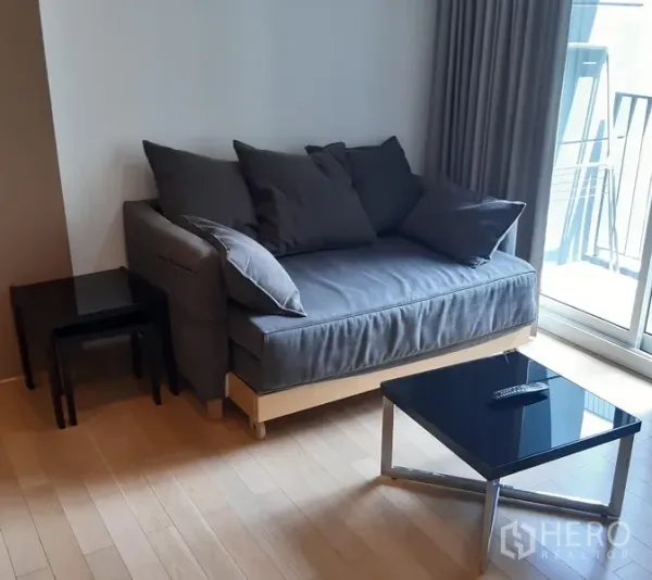 Condominium for rent in Khlong Toei, Bangkok - Bright Bangkok condo living room with grey sofa, glass coffee table, light wood floors and sliding door to a balcony.