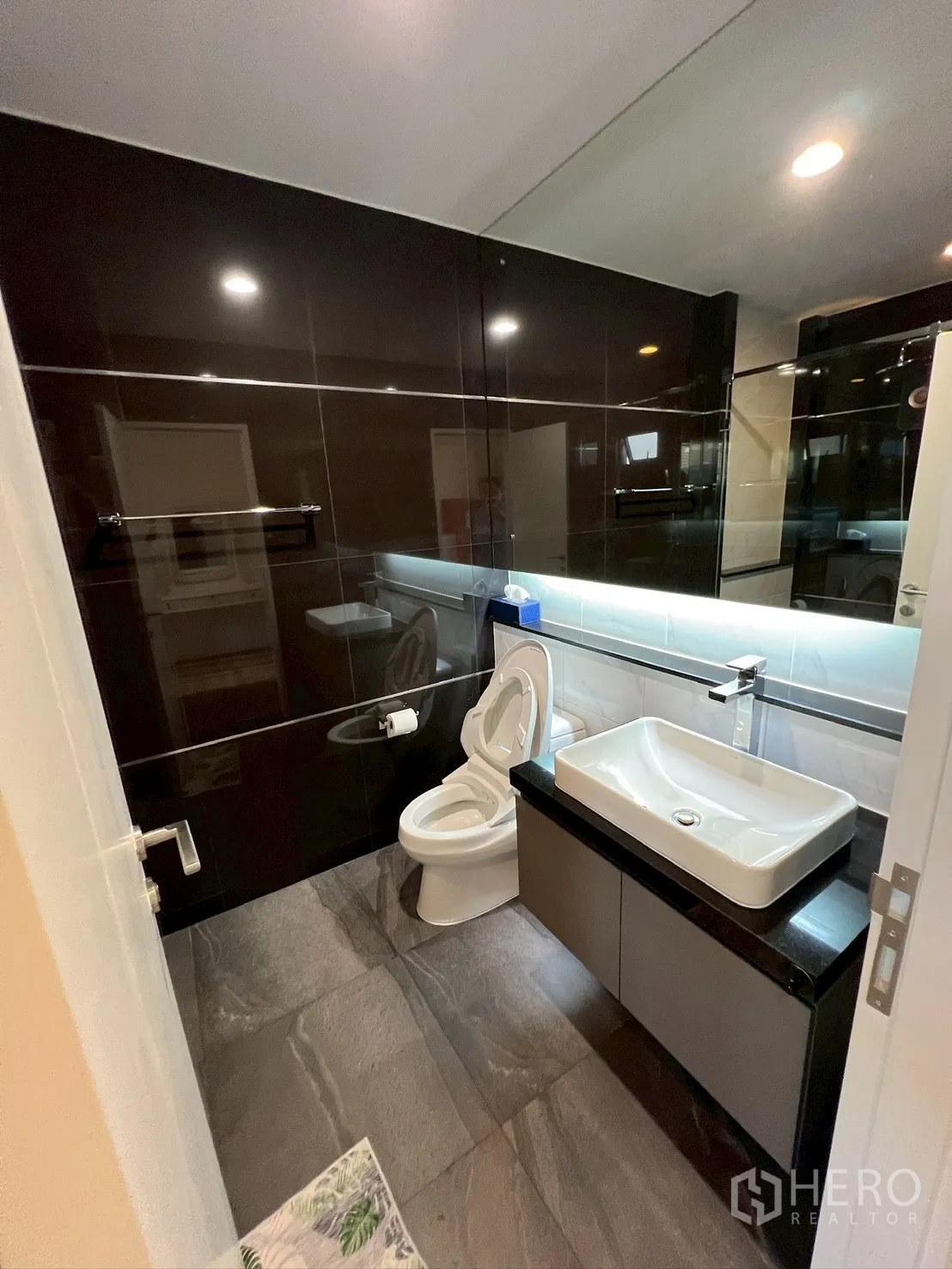 Detached House for rent in Bang Kapi, Bangkok - Modern bathroom with glossy black tiles, large mirror, sink vanity, and toilet.