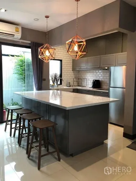 Townhouse for rent in Lat Phrao, Bangkok - Stylish kitchen with white stone island, pendant lights, stools, grey cabinets and garden access.