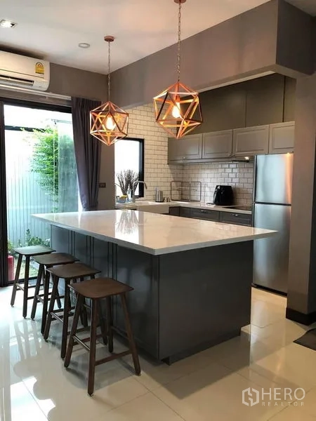 Townhouse for rent in Lat Phrao, Bangkok - Stylish kitchen with white stone island, pendant lights, stools, grey cabinets and garden access.