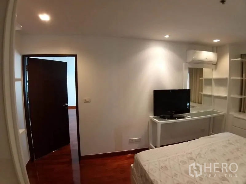 Condominium for rent or sale in Pathum Wan, Bangkok - Bedroom corner with work desk, mirror, TV and wall-mounted air conditioner.