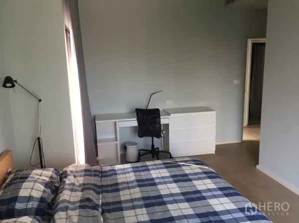 Condominium for rent in Bangkok - Spacious master bedroom with desk and chair, large window and light wood flooring.