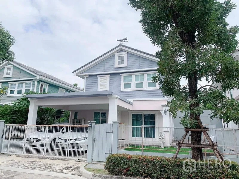 บ้าน ให้เช่าหรือขายในBang Phli, Samut Prakan - มุมหน้าบ้านอีกด้าน แสดงโรงจอดรถ 2 คันและสนามหญ้าหลังรั้วสี白