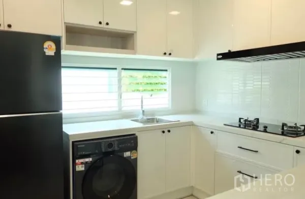 独立式住宅 出租在Bang Phli, Samut Prakan - 现代白色L形厨房，燃气灶、抽油烟机、水槽、冰箱与洗衣机。