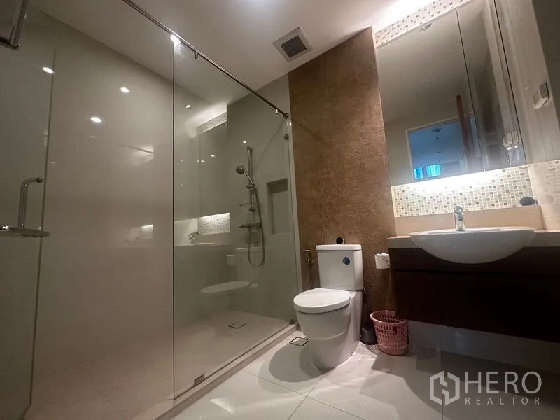 Condominium for rent in Khlong Toei, Bangkok - Bathroom featuring glass-enclosed shower, toilet and underlit mirror.