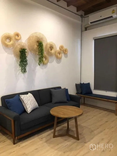 Detached House for rent in Phra Nakhon, Bangkok - Stylish lounge with dark sofa, round coffee table, wall decor, and wood-look flooring.