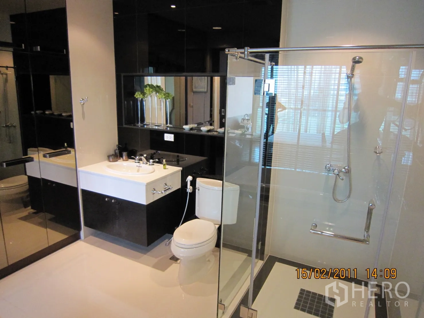 Condominium for rent or sale in Pathum Wan, Bangkok - Contemporary bathroom with glass‑enclosed shower, large mirror, vanity sink, and toilet.