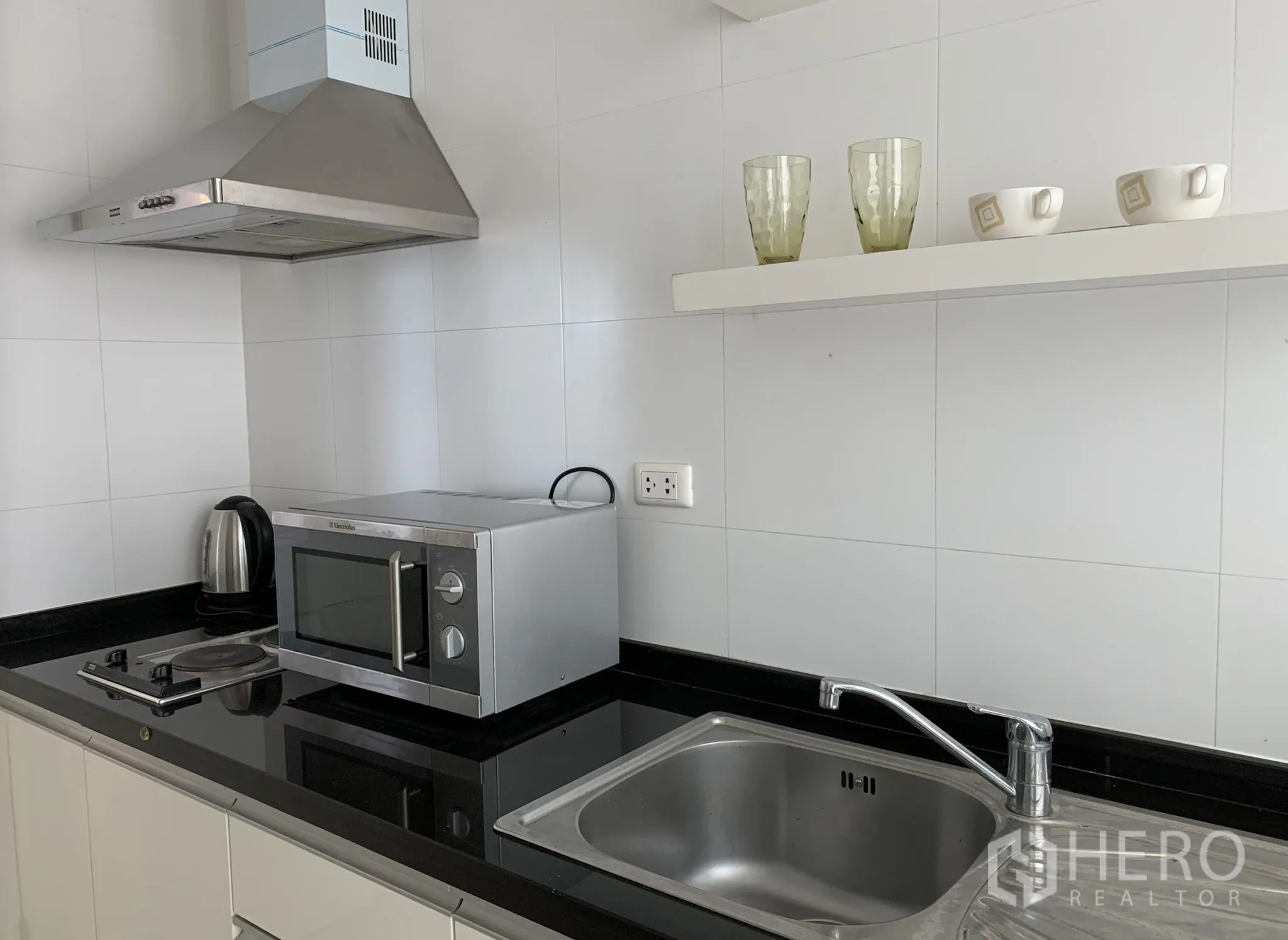 Condominium for rent in Khlong Toei, Bangkok - Compact kitchen with electric cooktop, range hood, microwave and stainless-steel sink.