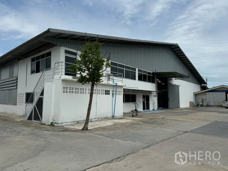 Warehouse for rent in Mueang Pathum Thani, Pathum Thani - Angled exterior of the warehouse showing long windows, metal roof, and broad internal driveway.
