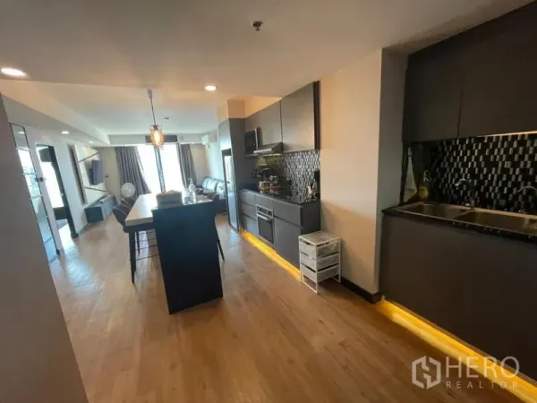 Condominium for sale in Chatuchak, Bangkok - Open-plan kitchen and living area with island, dark cabinetry, wood floors and a balcony city view at Supalai Park Phaholyothin.