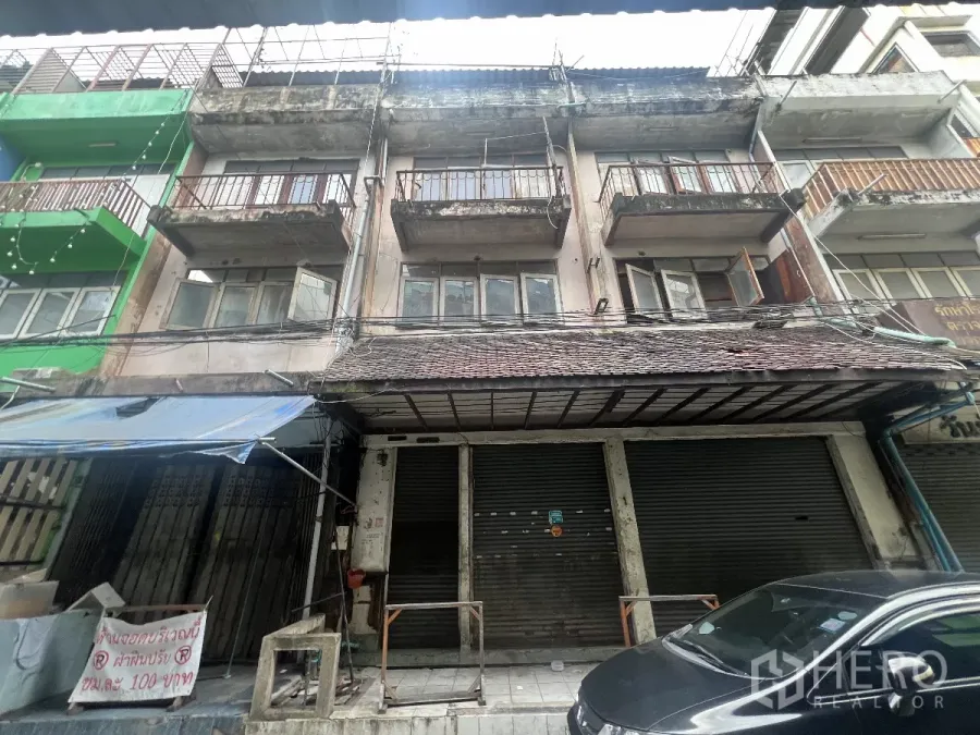 Shophouse for rent in Khlong Toei, Bangkok - Street-facing multi-storey shophouse facade with metal rolling shutters, balconies and awning in urban Bangkok.