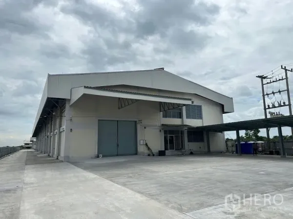 工厂 出租在Lam Luk Ka, Pathum Thani - 工厂外观，宽阔装卸雨棚、双扇推拉门与大片混凝土场地。