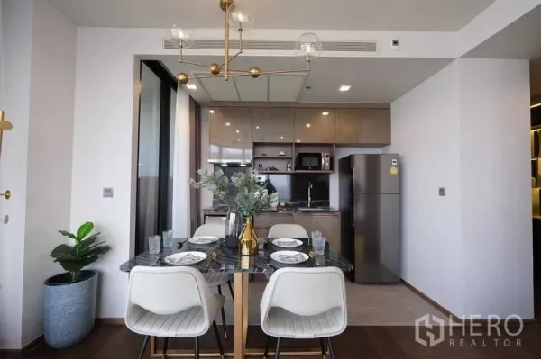 Condominium for rent in Khlong Toei, Bangkok - Modern dining room and open kitchen with brass chandelier and full-size refrigerator.